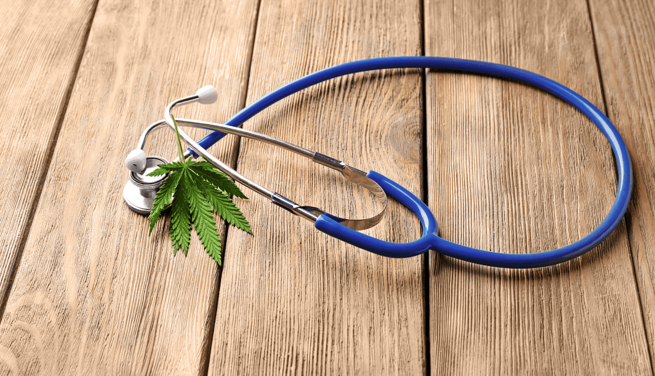 grünes Cannabis Blatt mit blauem Stethoskop auf Holztisch